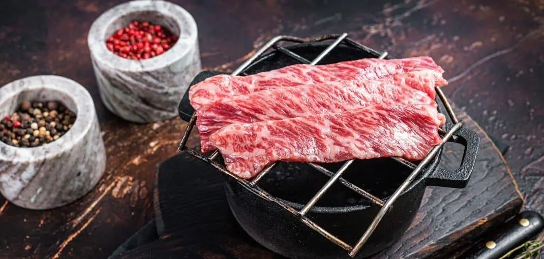 A selection of prime, raw, thinly sliced A5 grade Wagyu beef steaks beautifully arranged on a grill, showcasing the marbling characteristic of this high-quality meat. The vivid red color of the meat contrasts strikingly with the white marbling, promising a luxurious and flavorful culinary experience.
