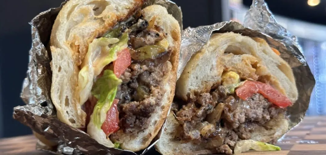 Gourmet ATL Chop sandwich featuring juicy ground Georgia wagyu, sautéed onions and peppers, fresh lettuce and tomato, and Tillamook cheddar, wrapped in foil.