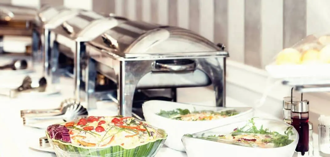 Catering setup featuring silver chafing dishes, fresh salads, and vibrant vegetable platters, ideal for holiday party dining by Frazie's Meat & Market.