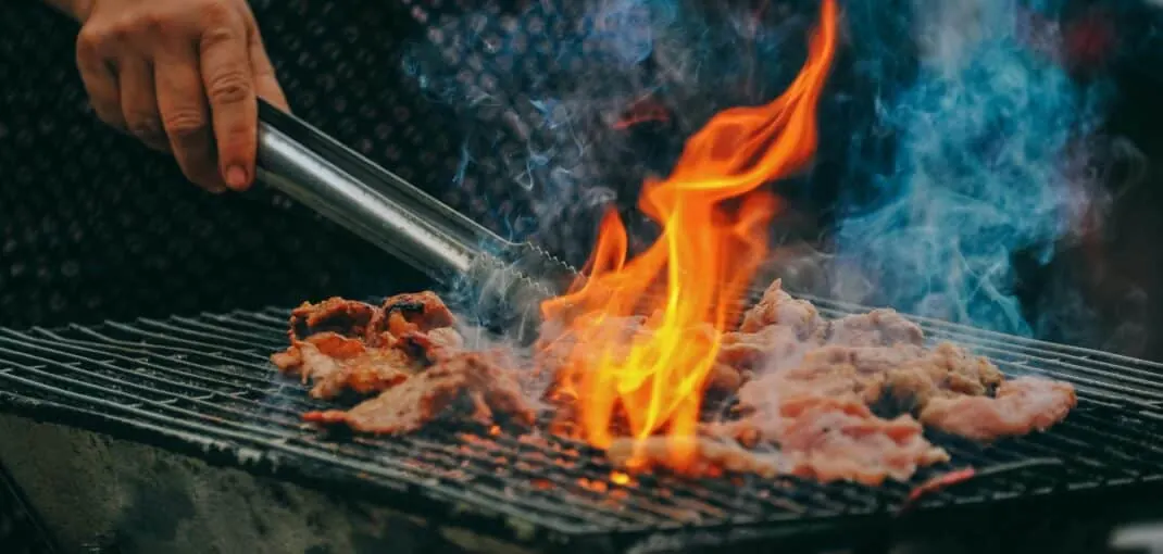 an adult male mastering the art of bbq by searing fresh steaks on an outdoor grill with flames coming up off the meat