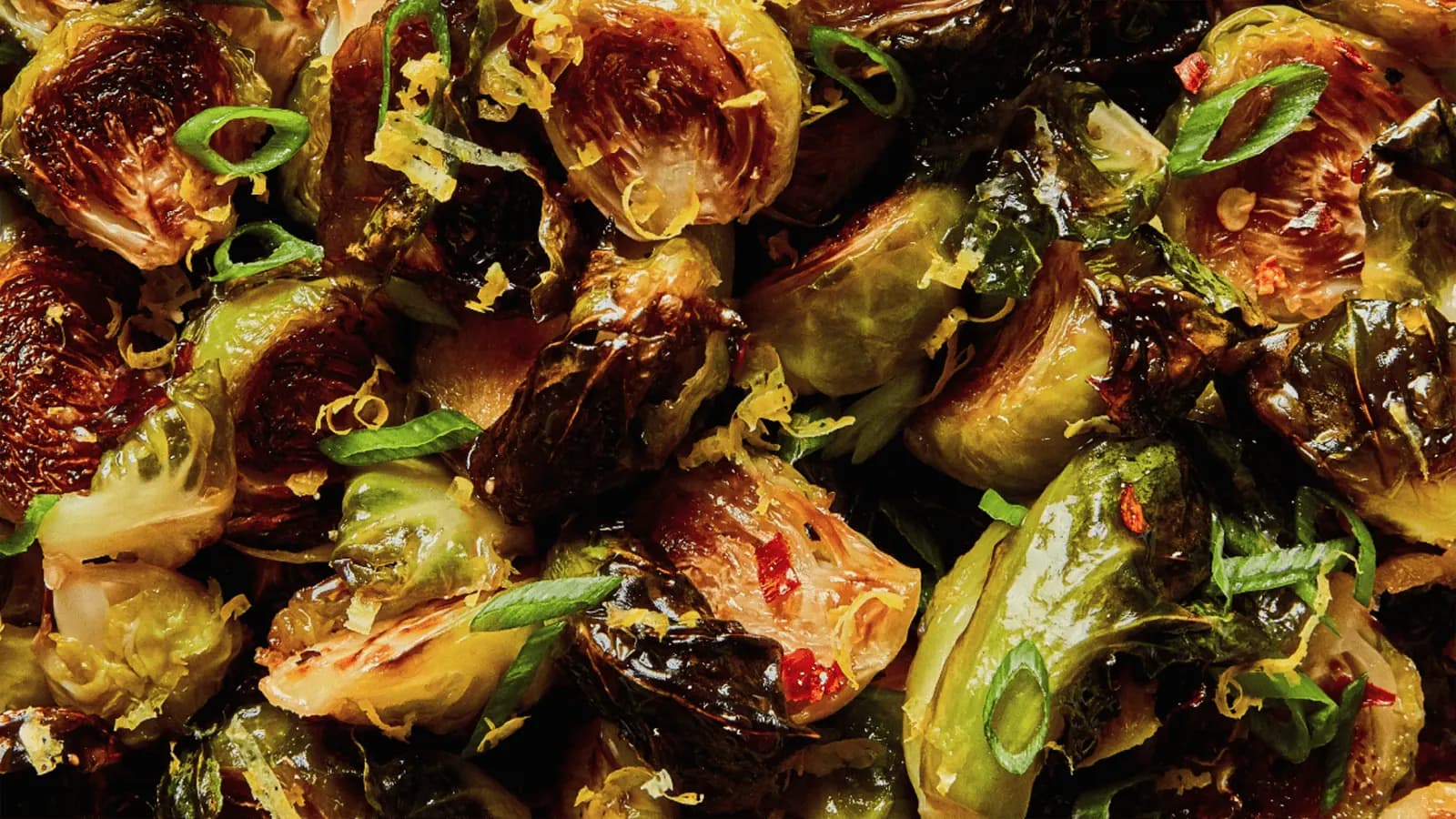 Roasted Brussels sprout halves in a serving dish, browned at the edges and scattered with green onion and lemon zest.