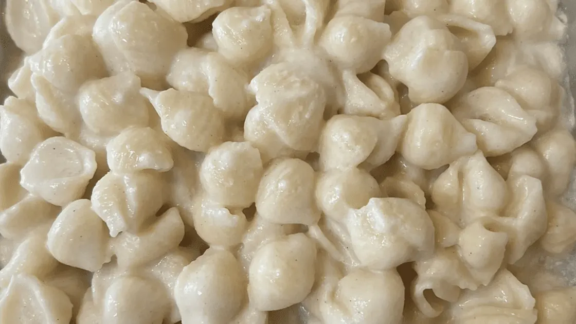 Creamy macaroni and cheese in a serving dish, the shells coated in a thick cheese sauce.