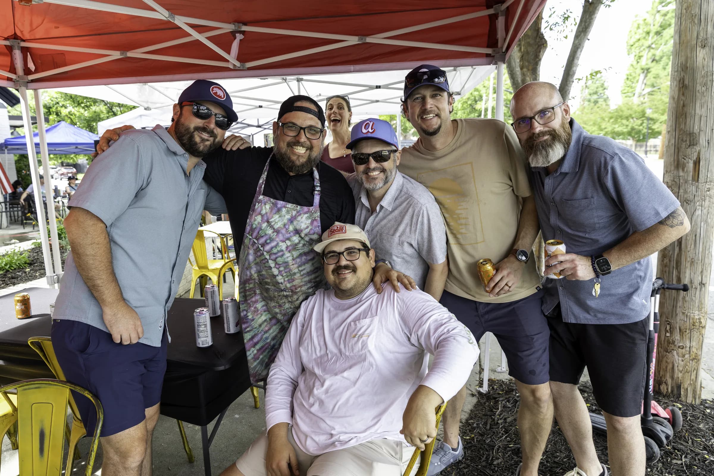 A group of customers and staff crowded together under Frazie's red canopy at the shop's third anniversary party, drinks in hand.
