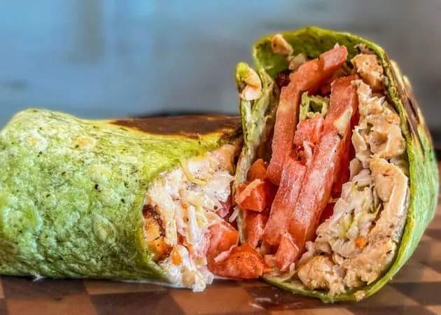 Green spinach wrap filled with shredded chicken, fresh tomatoes, and lettuce, showcasing a gourmet sandwich option from Frazie's Meat & Market in Atlanta.