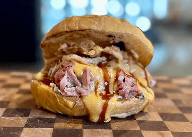 Gourmet sandwich featuring tender, sliced roast beef, melted cheddar cheese, crispy onions, and barbecue sauce, served on a toasted bun, highlighting Frazie's Meat & Market's artisanal offerings.