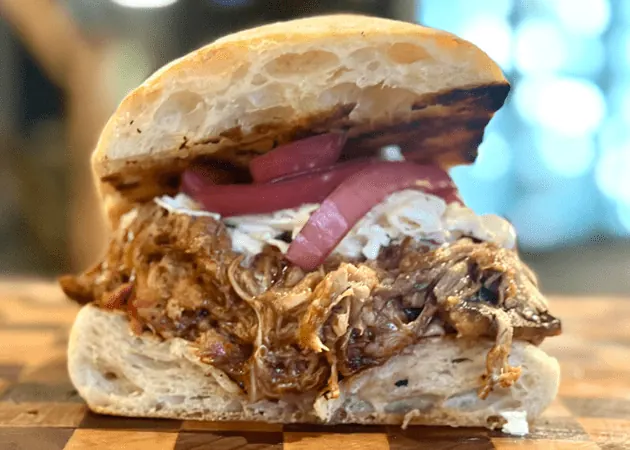 Pulled pork sandwich with coleslaw and pickled onions on a toasted bun, highlighting Frazie's Meat & Market's gourmet offerings in Atlanta.