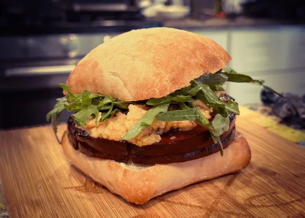 Hand-crafted sandwich featuring layers of eggplant, arugula, and creamy filling on a rustic ciabatta roll, highlighting Frazie's Meat & Market's gourmet offerings.