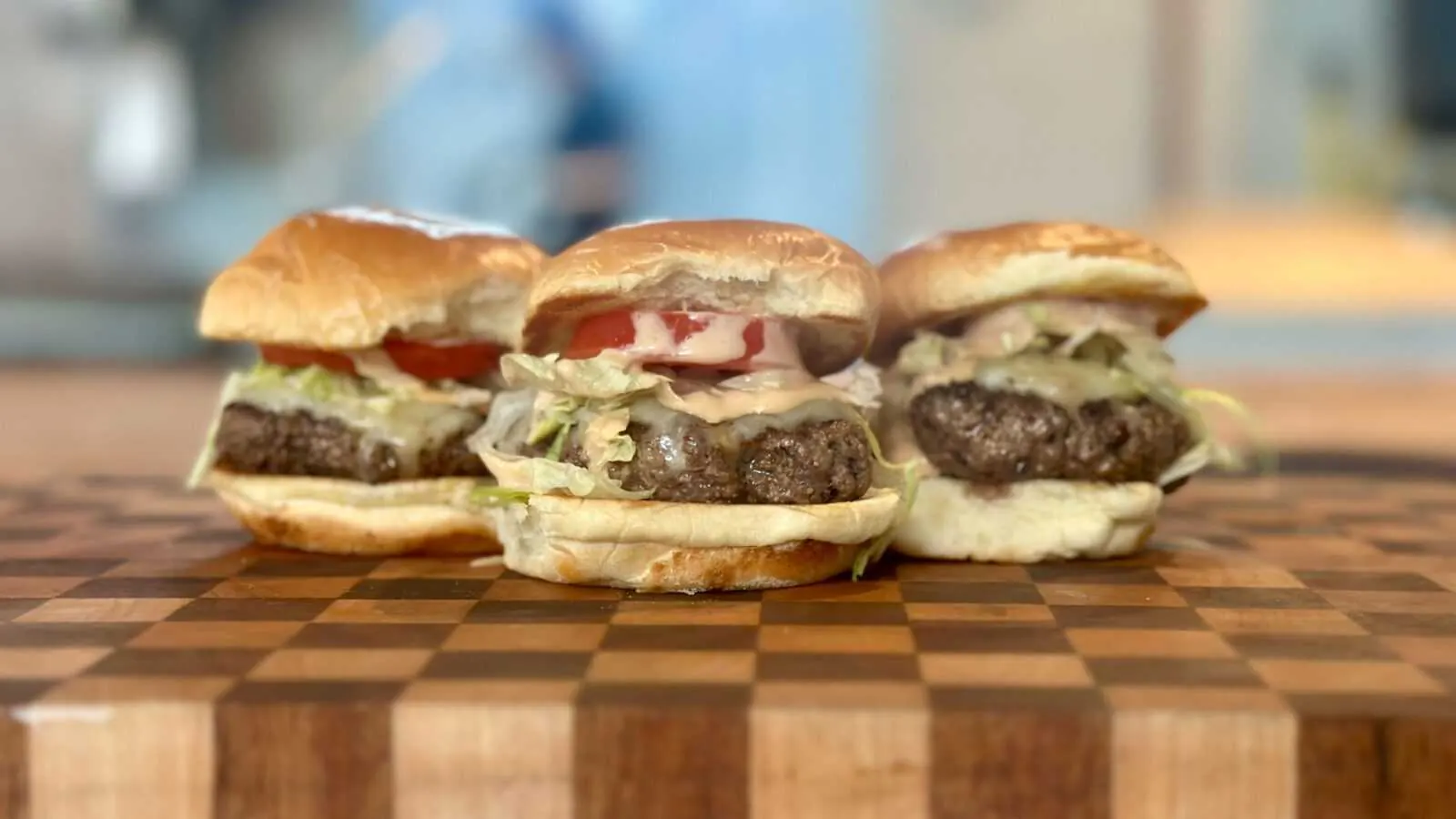 Beef and cheese sliders with house blend burger meat, sharp cheddar, fancy sauce, lettuce, and tomato on a wooden cutting board, highlighting Frazie's catering menu.