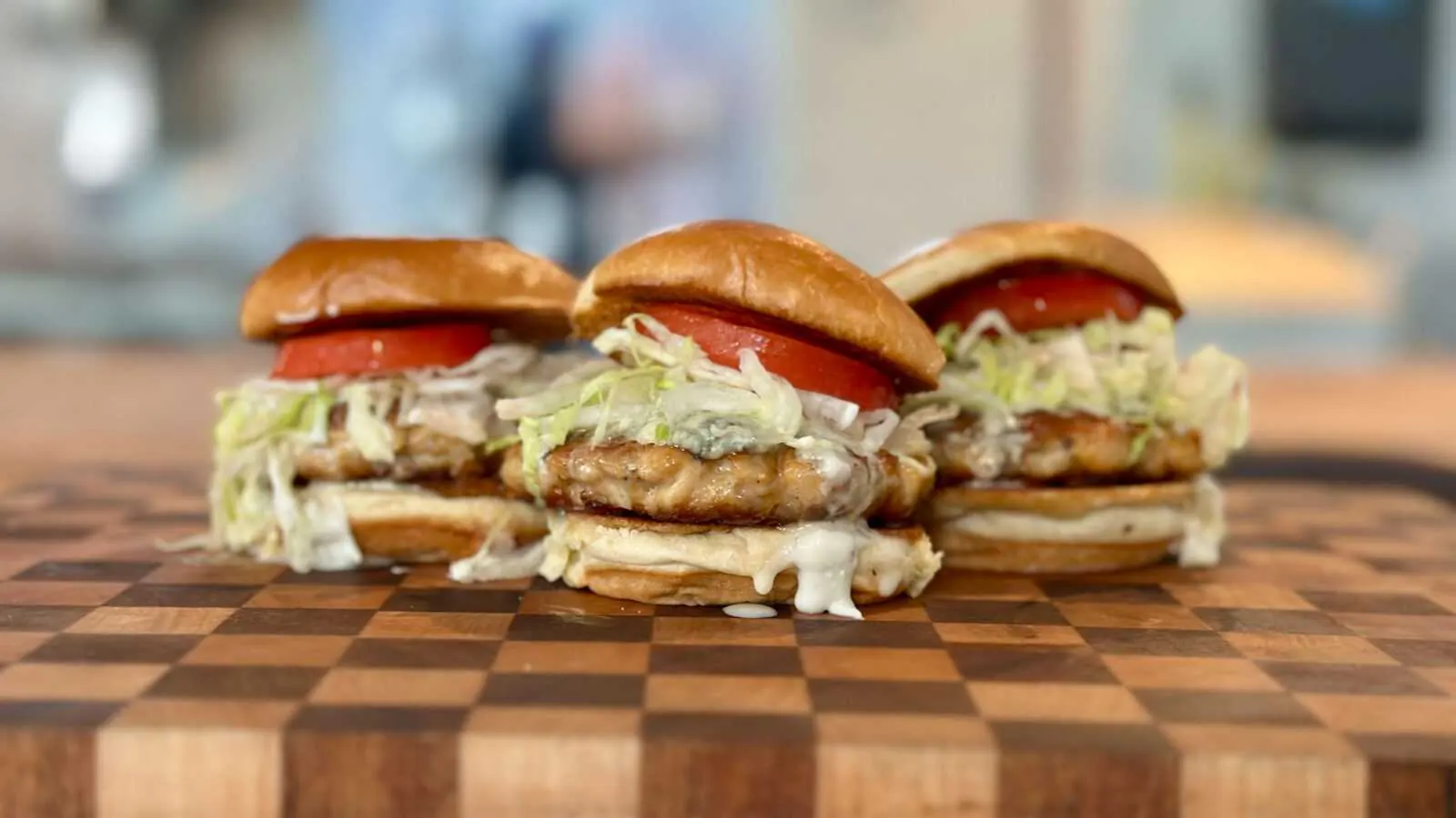 Buffalo chicken sliders with blue cheese, lettuce, and tomato on a wooden cutting board, showcasing Frazie's catering menu offerings.