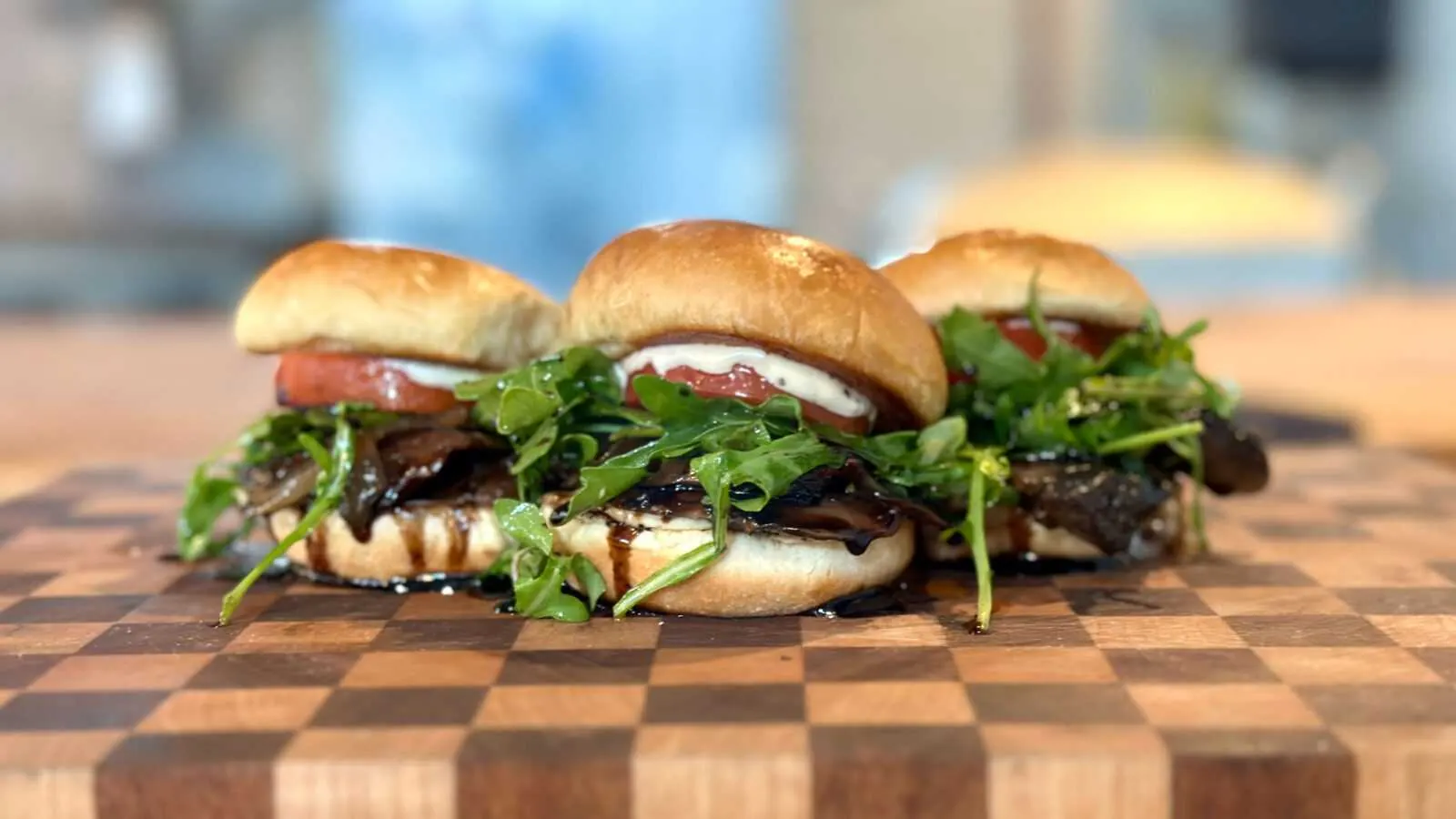 Flower Child Sliders featuring marinated portabella mushrooms, caramelized onions, arugula, Roma tomatoes, and roasted garlic aioli on a wooden serving board.