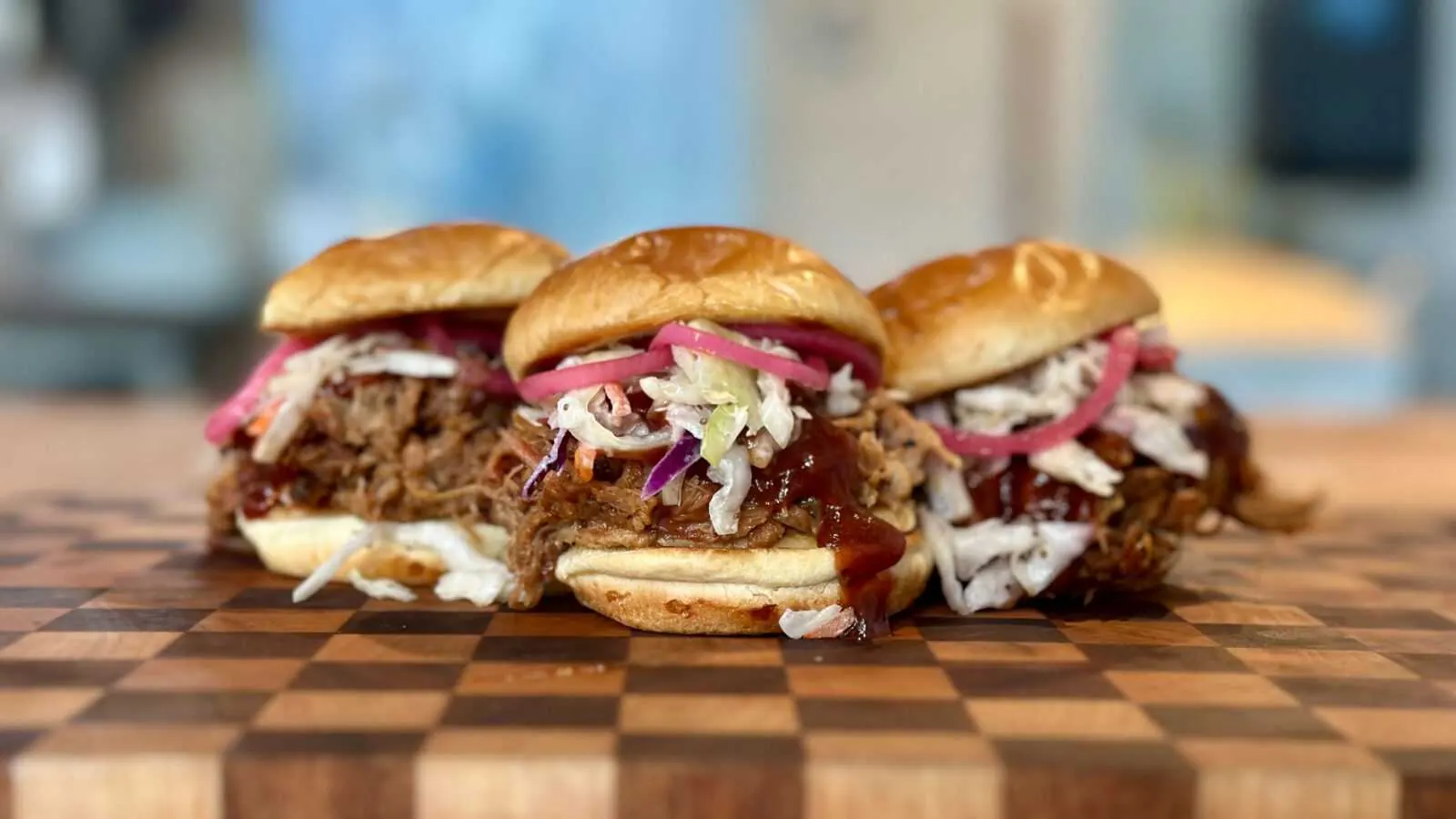Pulled pork sliders with country slaw and Frazie’s sauce on a wooden cutting board, showcasing gourmet catering options from Frazie's Meat & Market.