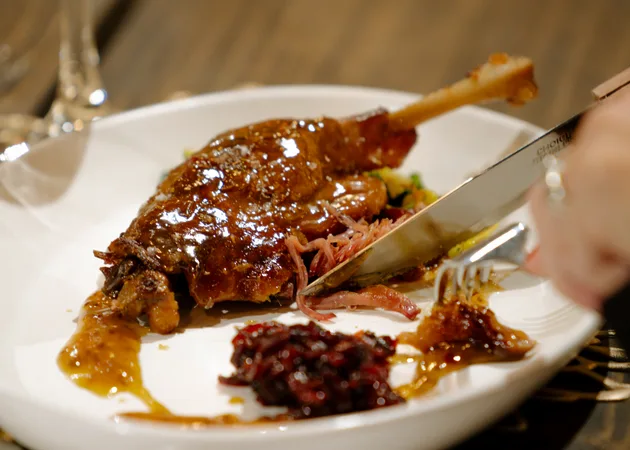 A glazed duck leg being carved at the table, served with pickled red cabbage, at a Frazie's supper club.