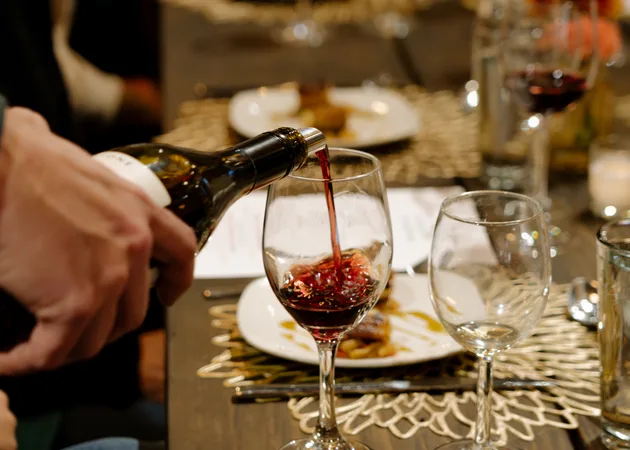 Red wine being poured into a glass at a Frazie's supper club, beside a plated course and candlelight.
